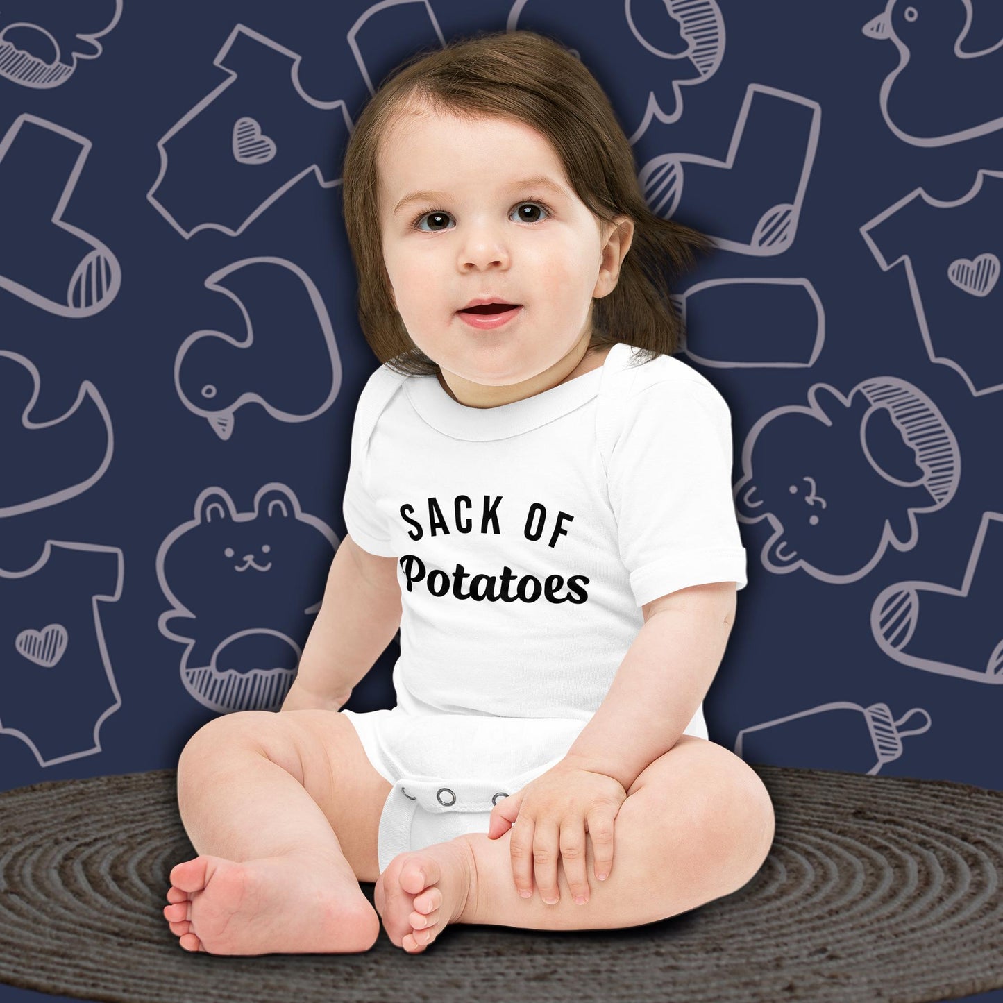 A cute baby with dark hair, sitting and looking forward, wearing a white Born Brash bodysuit that says 'Sack of Potatoes'. The background is dark blue with white doodle patterns of baby bodysuits, baby toys, and baby bottles. Perfect for a funny newborn gift or pregnancy announcement.