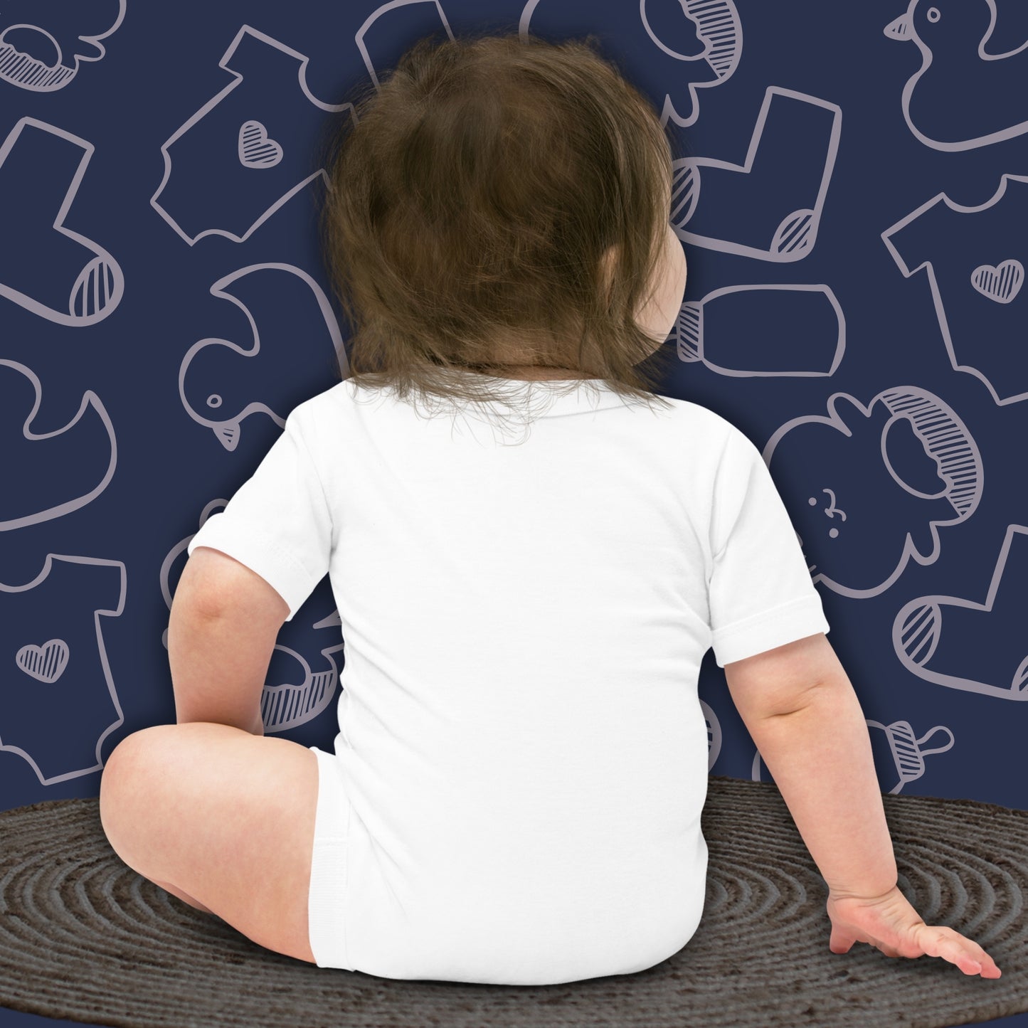 Back view of a baby wearing a funny, white bodysuit, sitting on a textured mat against a dark blue background with white patterns of humorous baby clothes and toys. Ideal for showcasing bodysuit fit and quality.