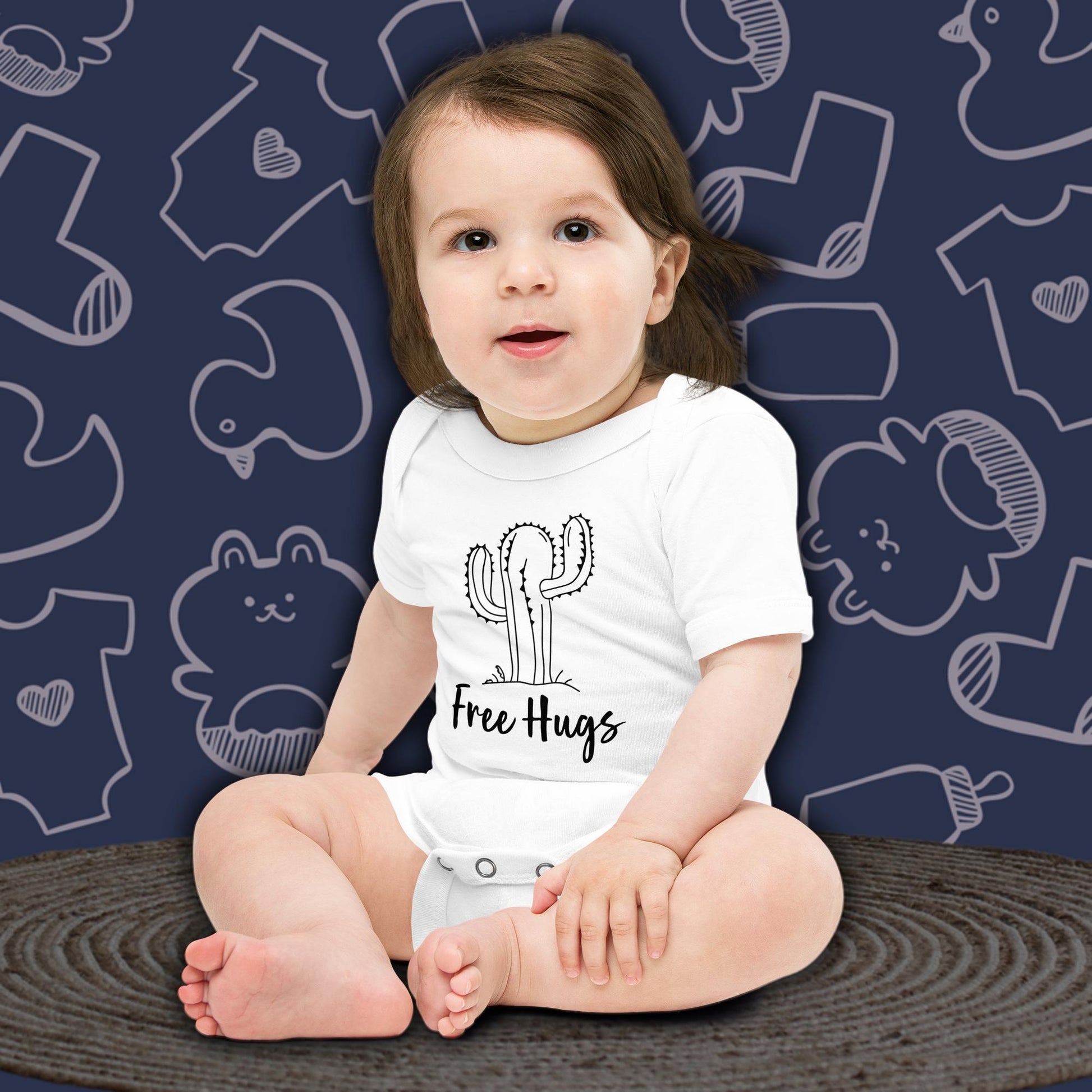A cute baby with dark hair, sitting and looking forward, wearing a white Born Brash bodysuit featuring a picture of a cactus and says 'Free Hugs'. The background is dark blue with white doodle patterns of baby bodysuits, baby toys, and baby bottles. Perfect for a funny newborn gift or pregnancy announcement.