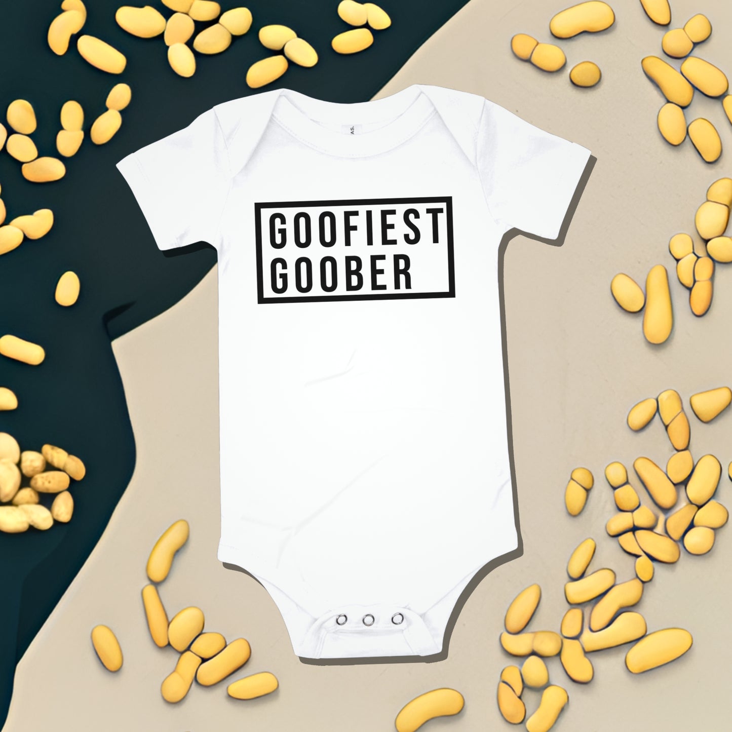 White baby bodysuit with "GOOFIEST GOOBER" text in a black box, surrounded by peanut illustrations. A funny humorous and quirky baby clothes design from Born Brash.