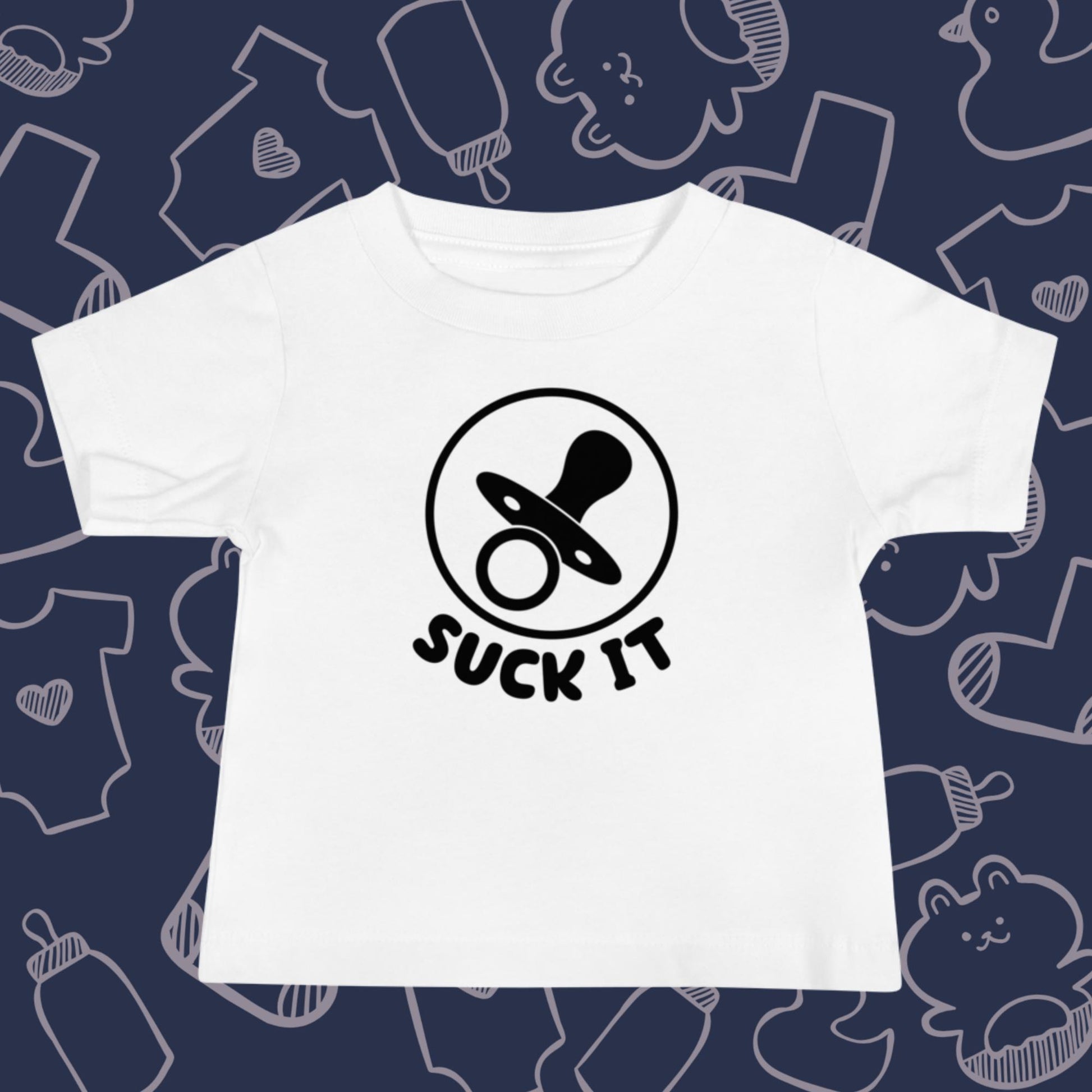 Funny, white baby t-shirt featuring an image of a pacifier and the playful text "SUCK IT" against a whimsical, blue backdrop of ducks, socks, stuffed animals, baby bodysuits, and bottles