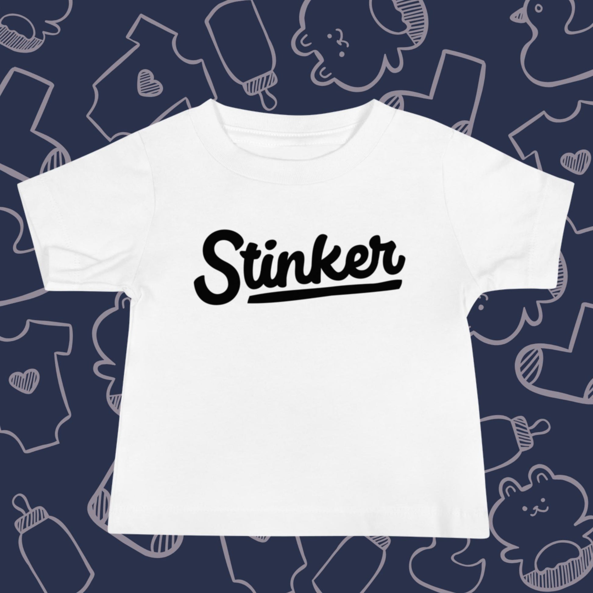 Funny, white baby t-shirt featuring the playful text "STINKER" against a whimsical, blue backdrop of ducks, socks, stuffed animals, baby bodysuits, and bottles