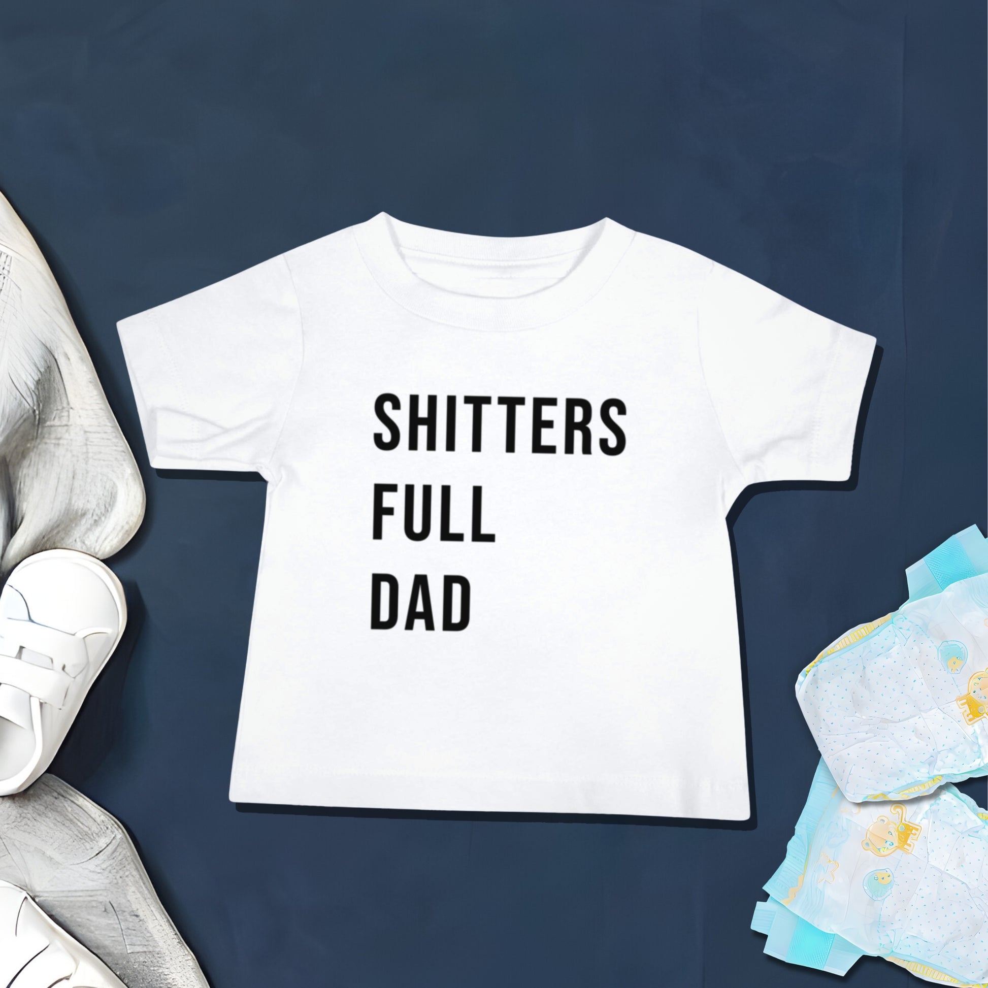 White baby t-shirt with "SHITTERS FULL DAD" text on a dark blue background with baby shoes and stacked diapers. A funny humorous baby t-shirt design about diaper duty, perfect as a new dad gift or funny baby shower gift from Born Brash.