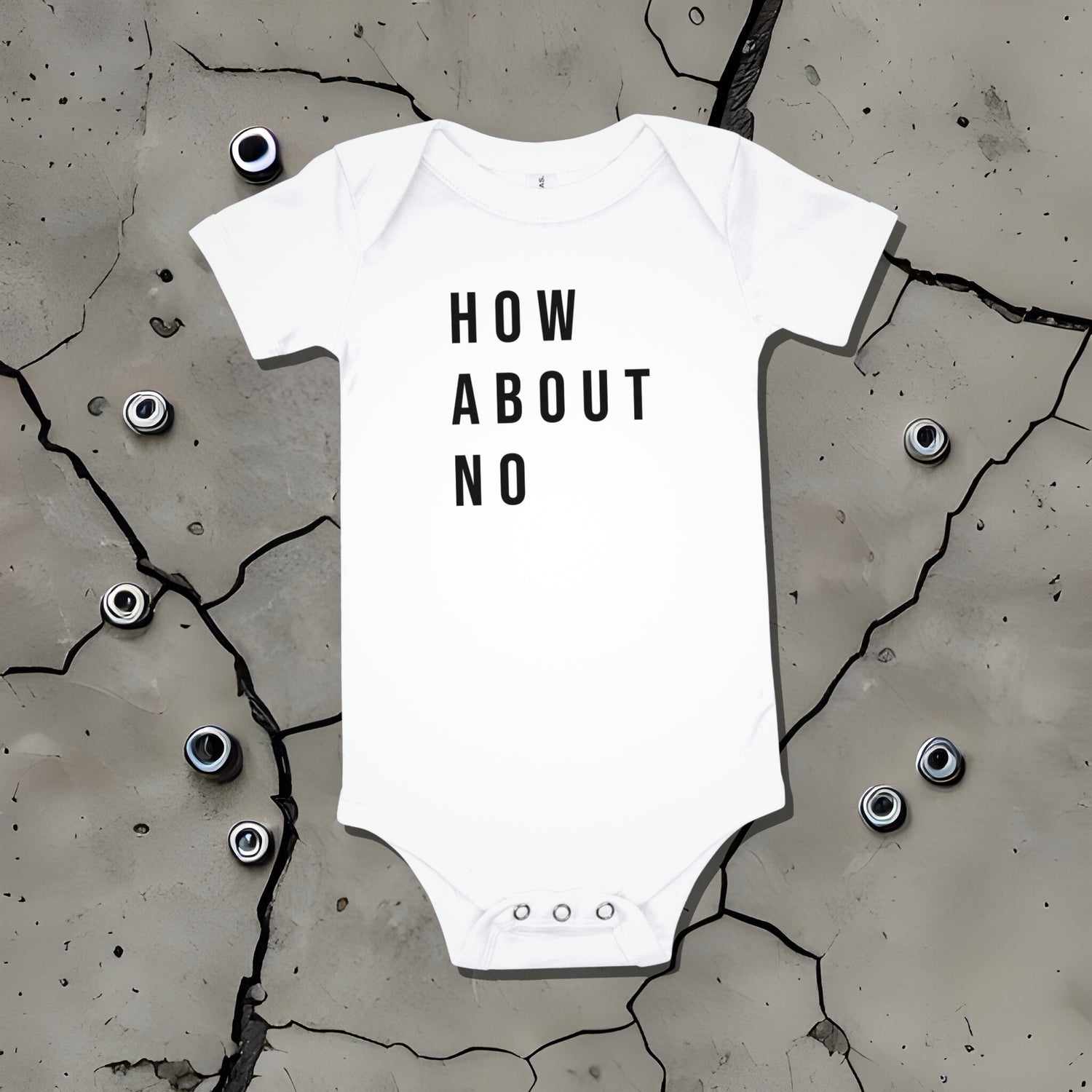 White baby bodysuit with "HOW ABOUT NO" text displayed on a cracked surface. A bold statement baby clothes design conveying sarcastic attitude from Born Brash.