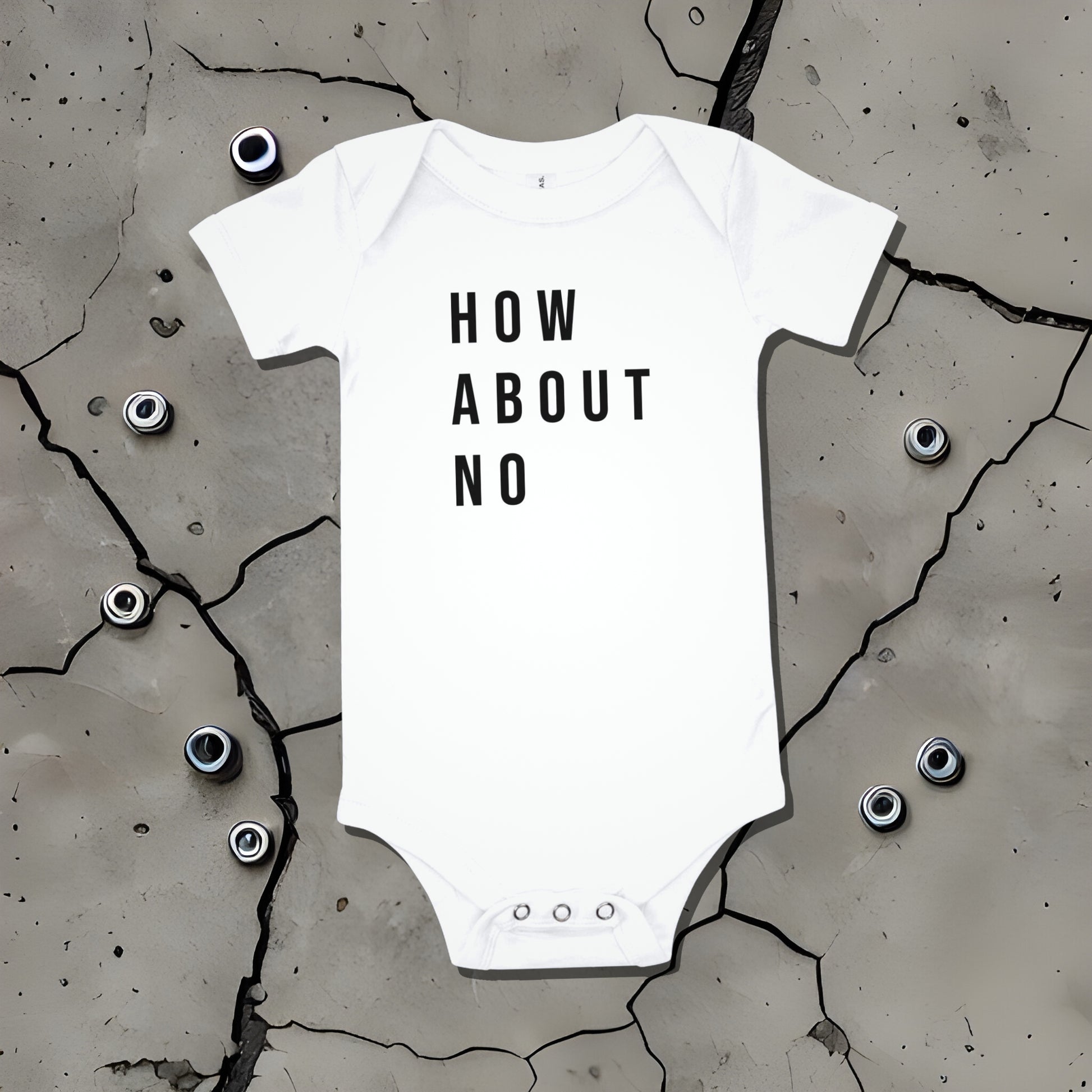 White baby bodysuit with "HOW ABOUT NO" text displayed on a cracked surface. A bold statement baby clothes design conveying sarcastic attitude from Born Brash.
