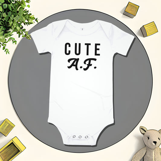 White baby bodysuit with "CUTE A.F." text on a gray circular mat with toy and plant illustrations. A bold attitude baby clothes design with a funny unapologetic statement from Born Brash.