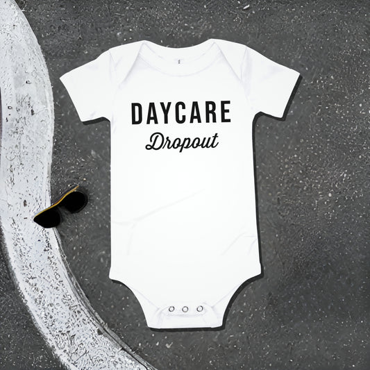 White baby bodysuit with "DAYCARE Dropout" text on an asphalt background with road line and sunglasses. A funny humorous and rebellious baby clothes design about daycare from Born Brash.