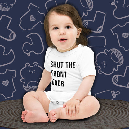 A cute baby with dark hair, sitting and looking forward, wearing a white Born Brash bodysuit that says 'Shut the Front Door'. The background is dark blue with white doodle patterns of baby bodysuits, baby toys, and baby bottles. Perfect for a funny newborn gift or pregnancy announcement.