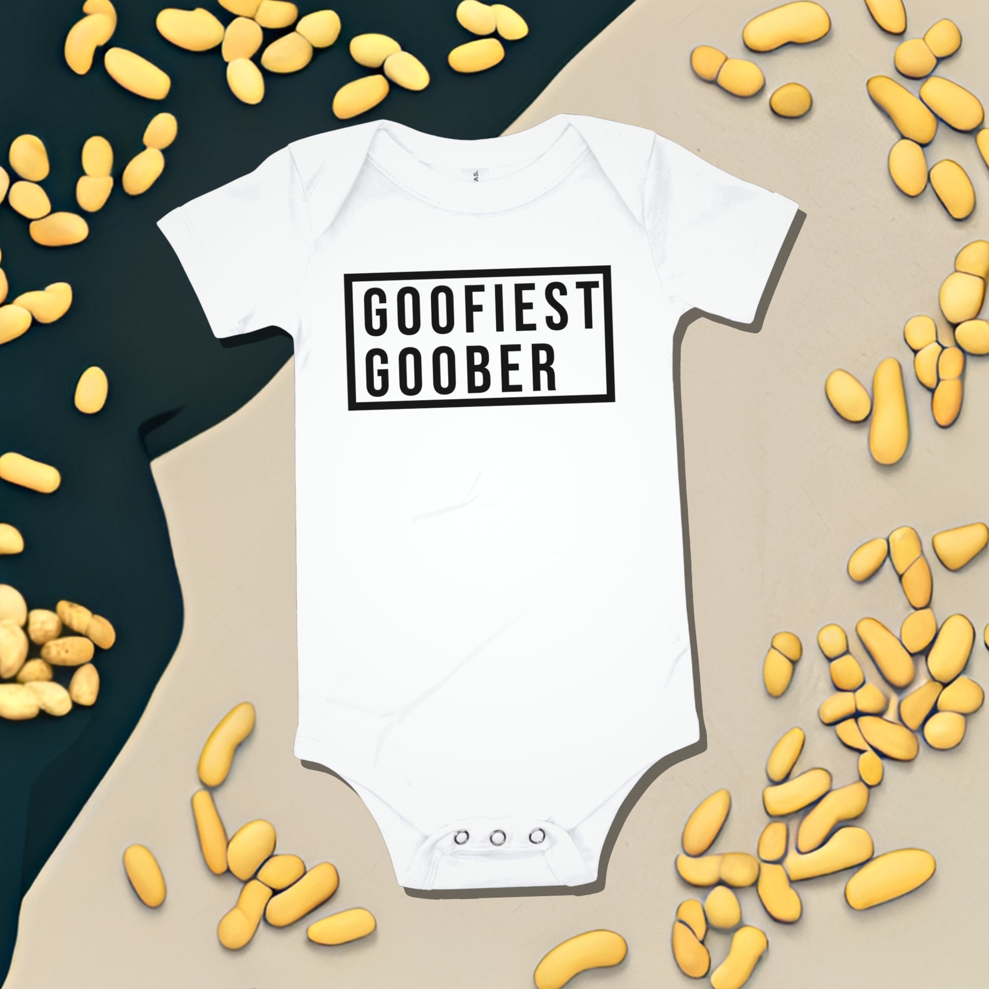White baby bodysuit with "GOOFIEST GOOBER" text in a black box, surrounded by peanut illustrations. A funny humorous and quirky baby clothes design from Born Brash.