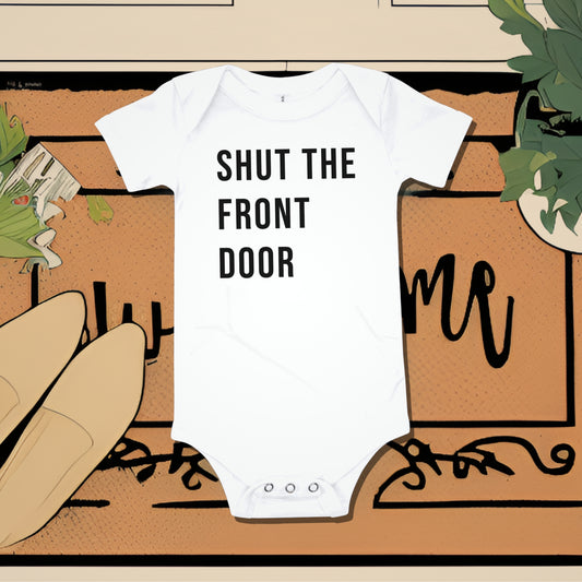 White baby bodysuit with "SHUT THE FRONT DOOR" text, placed on a welcome doormat. A funny humorous and sarcastic baby clothes design that makes a statement from Born Brash.