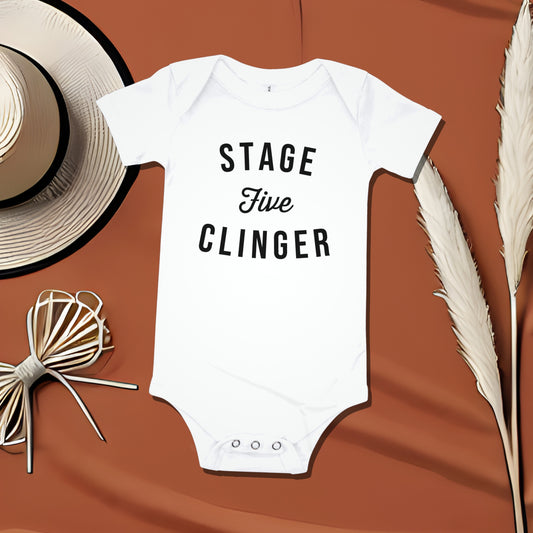 White baby bodysuit with "STAGE Five CLINGER" text on a brown background with a straw hat and feathery stalks. A funny humorous and relatable baby clothes design about clingy babies, a great baby shower gift from Born Brash.