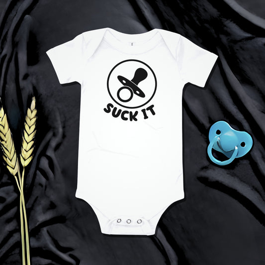White baby bodysuit with a pacifier graphic and "SUCK IT" text on a dark background with a pacifier and wheat. A funny humorous and irreverent baby clothes design from Born Brash.