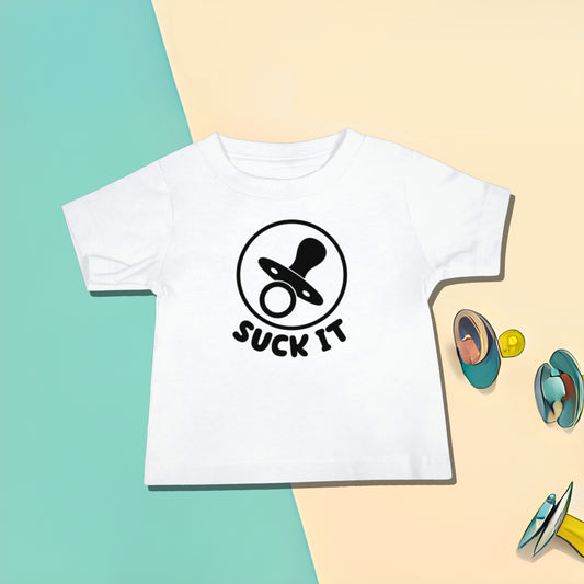 White baby t-shirt with a pacifier graphic and "SUCK IT" text on a split background with scattered pacifier illustrations. A funny humorous irreverent baby t-shirt design about pacifiers, making it a great baby shower gift from Born Brash.