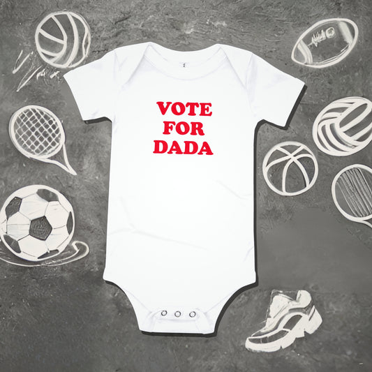 White baby bodysuit with "VOTE FOR DADA" in bold red text, surrounded by sports sketches. A funny humorous baby clothes design and perfect new dad gift from Born Brash.