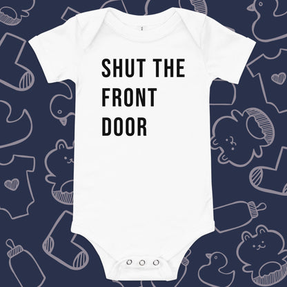 Funny, white baby onesie featuring the playful text "SHUT THE FRONT DOOR" against a whimsical, blue backdrop of ducks, socks, stuffed animals, baby bodysuits, and bottles