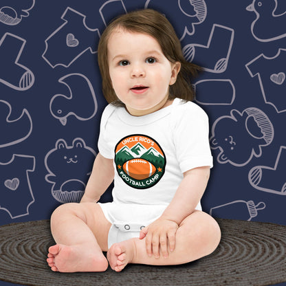 A cute baby with dark hair, sitting and looking forward, wearing a white Born Brash bodysuit that says 'Uncle Rico's Football Camp' with an illustration of a football and mountains. The background is dark blue with white doodle patterns of baby bodysuits, baby toys, and baby bottles. Funny football themed baby clothes. Perfect baby gift for football fans or Napoleon Dynamite fans.