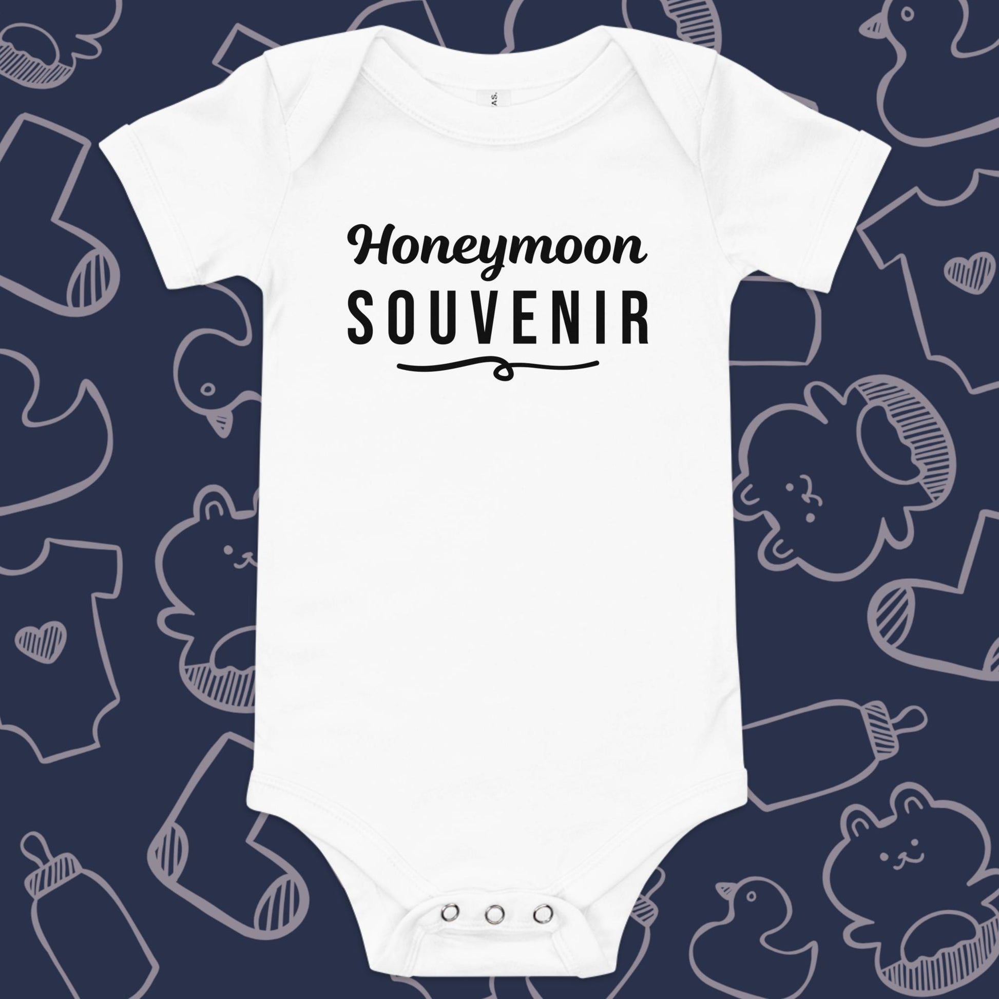 Funny, white baby bodysuit featuring the playful text "Honeymoon Souvenir" underlined against a whimsical, blue backdrop of baby toys, bodysuits, and bottles.