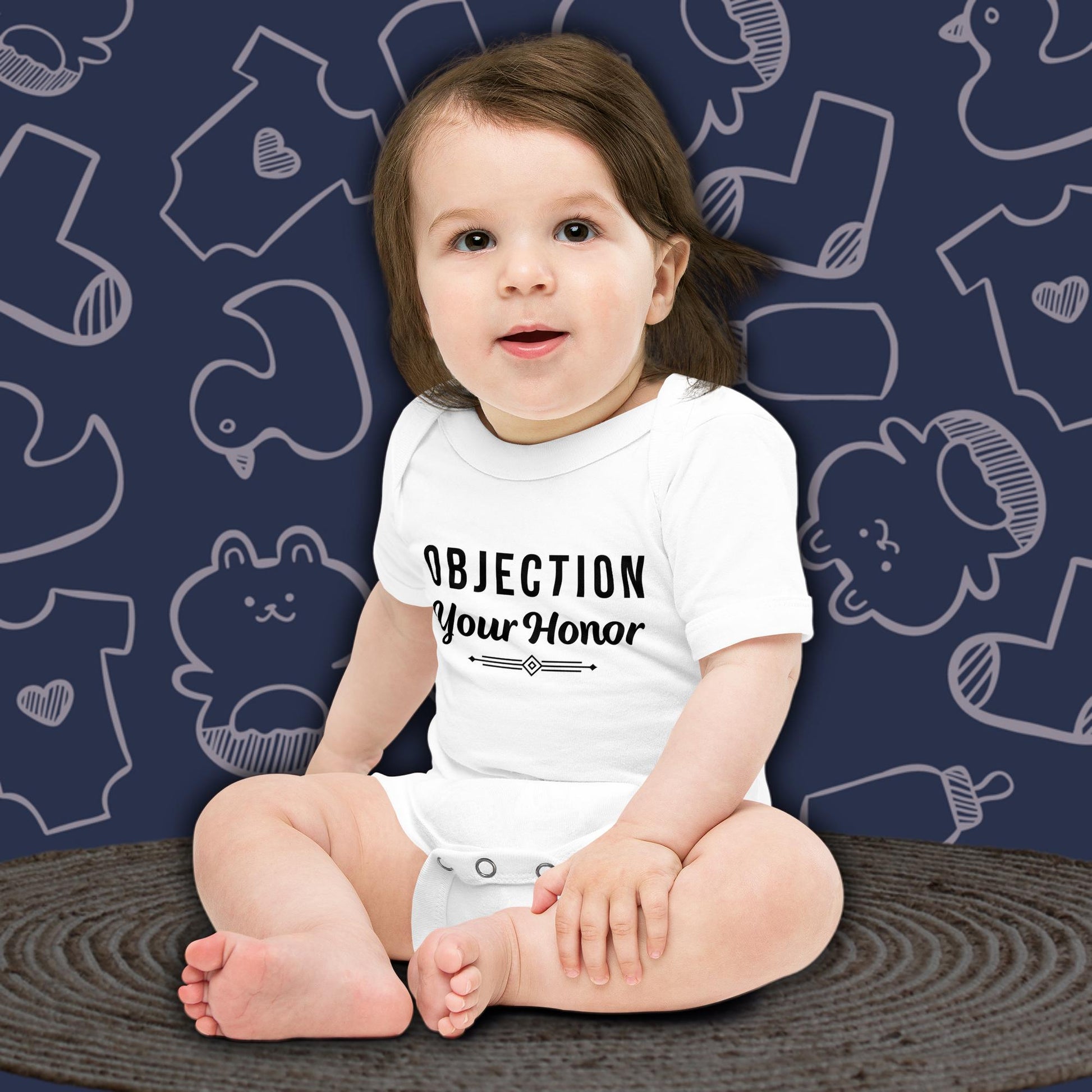 Baby wearing a funny white bodysuit with 'OBJECTION Your Honor' text against a blue background with baby clothing illustrations.