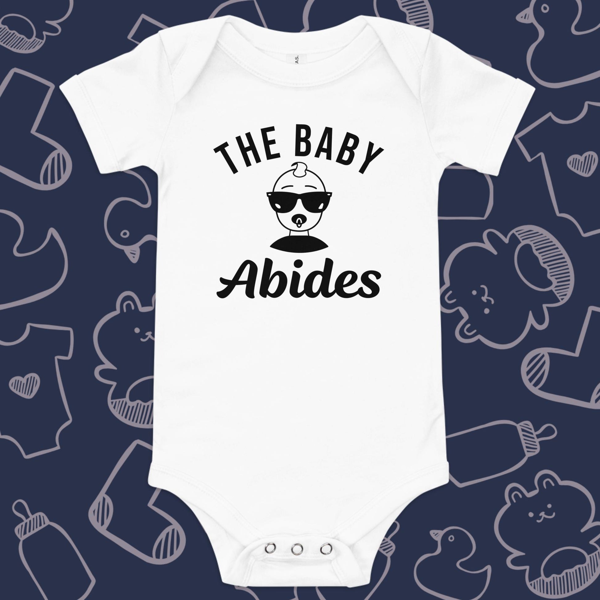 Funny, white baby bodysuit featuring the playful text "The Baby Abides" and an illustration of a cool baby wearing sunglasses against a whimsical, blue backdrop of baby toys, bodysuits, and bottles.